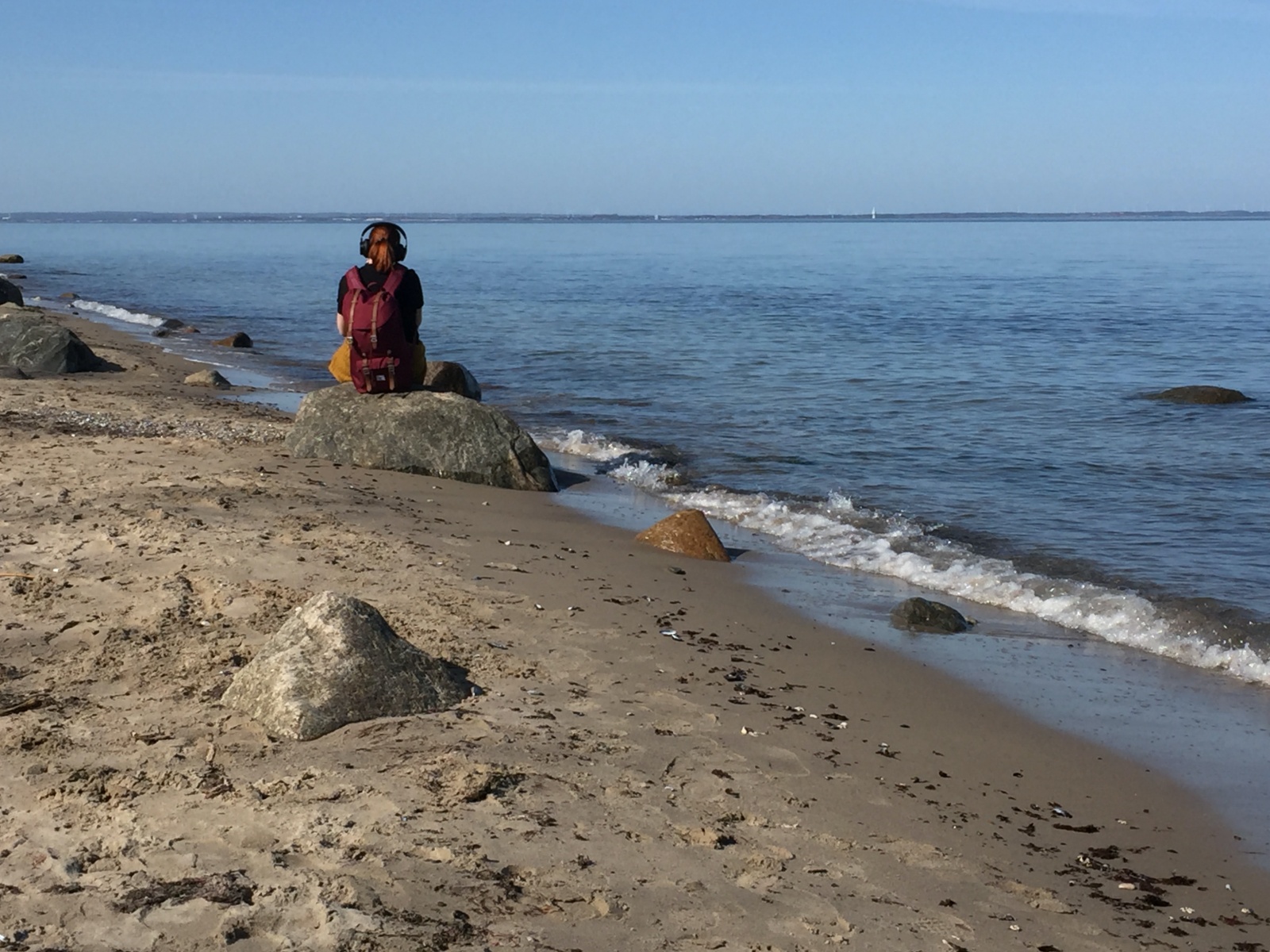 Eine Frau sitzt am Strand auf einem Stein