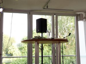 Ein Blick auf ein Lesepult, einen Lautsprecher und dahinter aus dem Fenster auf eine Wiese